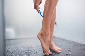 Woman shaving legs in shower using razor for smooth, hair-free skin. Shaving routine with water and moisture, ideal for promoting shave oil or skincare for sensitive skin.